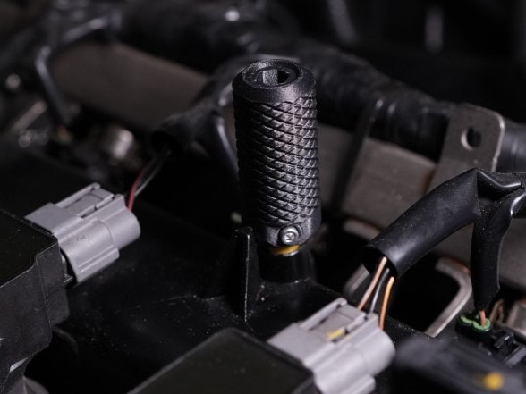 A black knurled PET-CF part fitted among cables in an engine bay