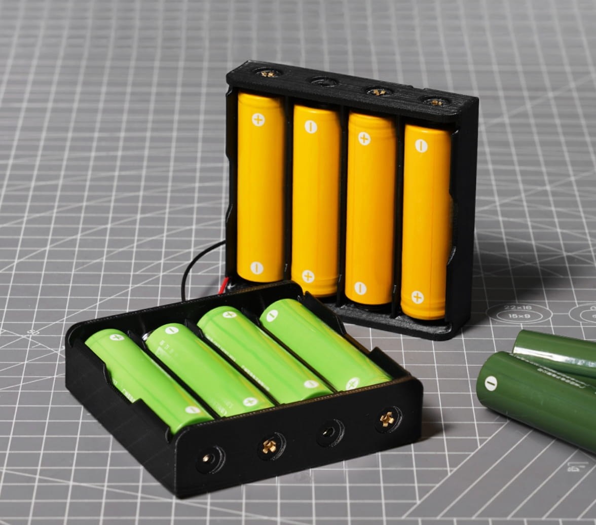 Two black PC FR battery boxes holding cylindrical cells, on a cutting mat