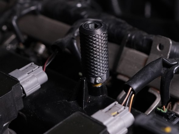 A black knurled PET-CF part fitted among cables in an engine bay